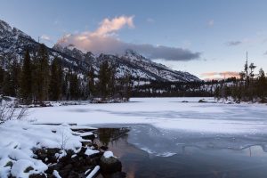 Ice overtaking the majority of Taggart Lake's calm waters below the Teton Mountains. Grand Teton National Park, Wyoming