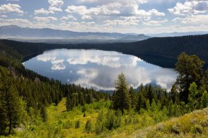 Phelps Lake reflecting a partly cloudy sky below surrounding forests and the Valley Trail. Grand Teton National Park, Wyoming