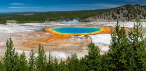 The colorful waters of Grand Prismatic Spring glowing among the other Midway Geyser Basin features, such as Excelsior Geyser Crater beyond. Yellowstone National Park, Wyoming