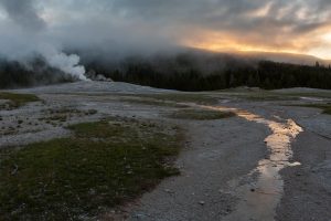 Water runoff from Old Faithful Geyser flowing below fog lifting from the distant hill at sunrise. Yellowstone National Park, Wyoming